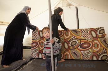 Two women put away mattresses and blankets in the tent while a young boy looks on