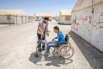 A Mercy Corps team member works with a young man who uses mobility equipment at a refugee camp in Jordan