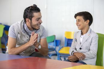 At a youth center in Zaatari, Omar Al-Tal sits with Mohammad. Mohammad is able to play sports and games while learning important life skills like computers and English. Two of Mohammad’s favorite activities are playing foosball and soccer, but his favorite is singing. At a recent talent show in the center, he finished third. Photo: Ezra Millstein/Mercy Corps