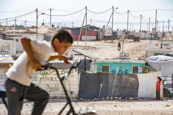 Boy on a bike with refugee camp in background