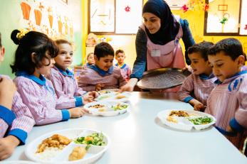 A woman carrying a tray serves lunch to students in lebanon