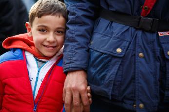 A young boy smiles and holds the hand of the adult next to him