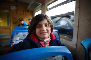 A young girl looks over her seat on the train, smiling softly