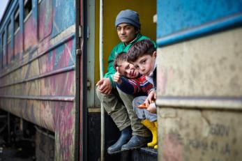 Three young boys sit on the stairs on a train car