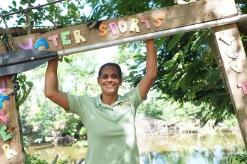 Christina holding a canoe paddle above her head and smiling beneath a sign that reads water sports eco tours
