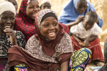 A girl sitting on the ground with other girls nearby, all laughing, in Nigeria