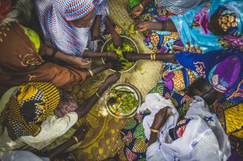 Women in colorful clothing reaching in to share food from a bowl at center in Niger. Photo: Sean Sheridan for Mercy Corps