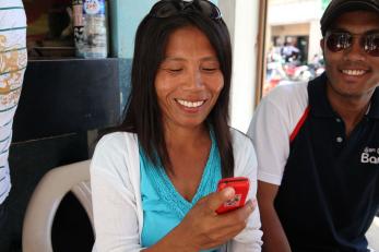 A woman smiles while holding her phone and making a mobile banking transaction.