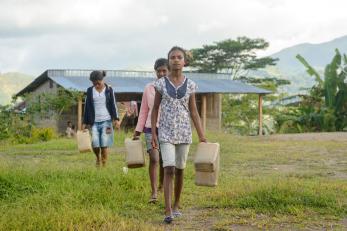 Three girls carrying plastic jugs of water