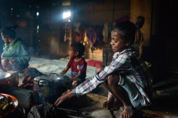 A girl feeding a cooking fire in timor-leste with family nearby