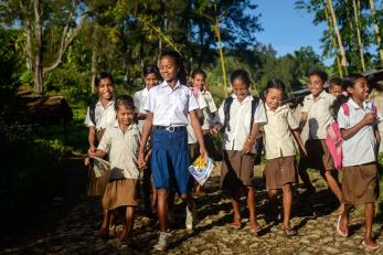 Children in school uniforms walk along a rocky path to school