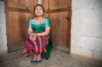 Young woman sitting in corner of room, in front of two doors.