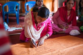 Woman writing on large sheet of paper with group behind.