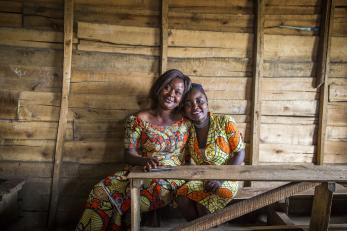 A mother and daughter sit together on a wood bench.