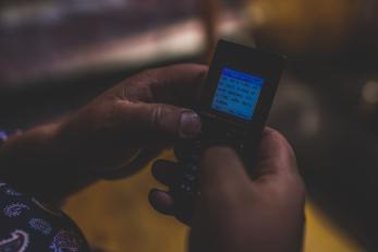 A pair of hands uses a mobile phone to send an SMS text. 