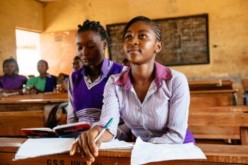 A high school student in Nigeria leans forward in their seat inside a classroom with students. 