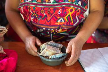 The hands of a savings and loan group grasp a bowl of paper money in Acul, Guatemala.