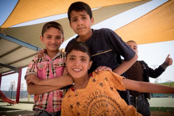 Four smiling young people gather for a group photo in a playground.