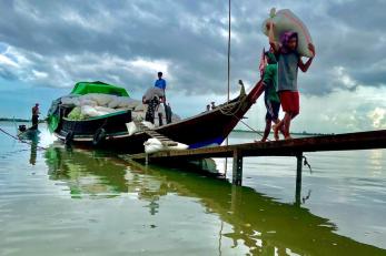 People carry fishing gear from a boat docked under a cloudy sky.