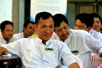 A person sits attentively while surrounded by other people in Myanmar. 