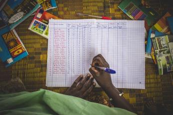 A hand holding a pen marks a paper spreadsheet.