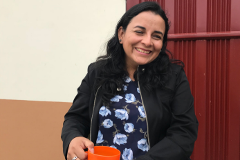 An adult sits in a chair smiling and holding a beverage mug. 