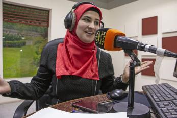 A person wearing headphones speaks into a microphone inside a broadcast studio in Jordan.