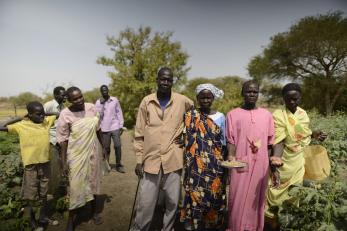 A group of people stand outside together holding harvested agricultural goods in South Sudan.