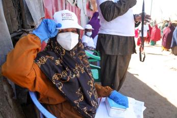 A person wearing face mask shows off their Mercy Corps hat to the camera on a busy street in Somalia.