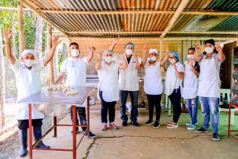 A group of bakers wave at the camera from an outdoor kitchen.