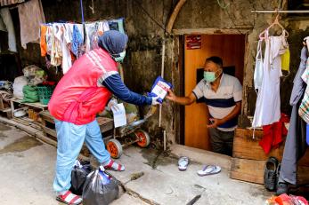 A Mercy Corps staff team member hands someone a hygiene kit during a door to door community outreach event in Jakarta Province.