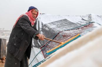 A person uses a broom to try and clear the snow away from their damaged tent.