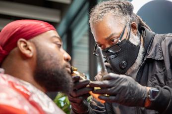 A barber trims the beard of a customer.
