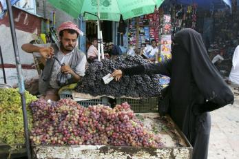 A person buys fruit at a market from a vendor.