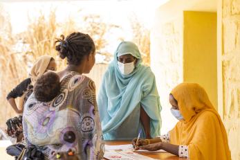 A person carrying a child speaking with two people at a table completing forms.