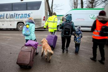 Emergency aid workers escorting women, children, and a dog to vehicles.