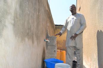 A person standing next to a tap in their compound connected to the local water facility.