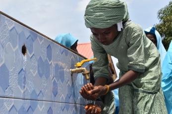 A young person washing their hands from a spigot.