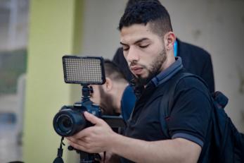 A photographer adjusts the settings on a camera mounted to a tripod.