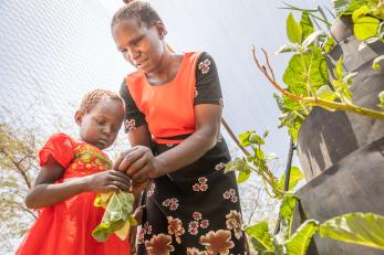 A mother teaching her daughter to pick vegetables from their garden.