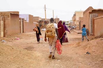 Sudanese community members walk down local street with baggage.