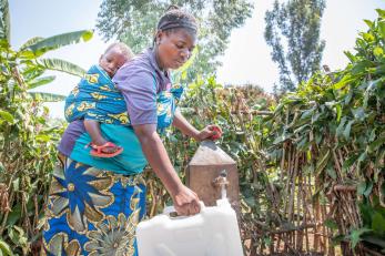 A farmer and mother collects water with her 1 year-old son