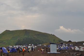 Families move about a camp with temporary living structures.