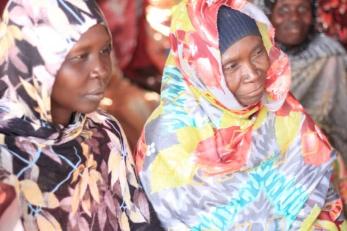 Two people sitting together listening to someone speak at a gathering..