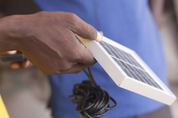 A hand holding a solar panel with a power chord hanging from it.