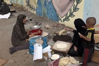 Two women in Gaza prepare flatbread while a child looks on