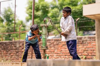 Two Nepalese students work and use a water pump together.