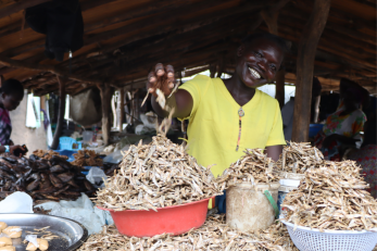 Ugandan woman stands in her shop smiling.