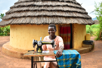 A GIRL-H participant poses with a tailoring machine she purchased through her participation in the GIRL-H financial inclusion interventions.