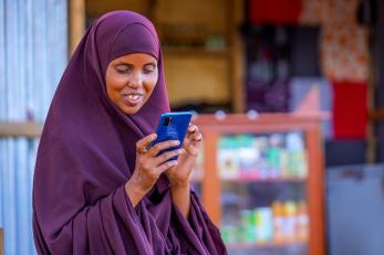 Kenyan woman working on her mobile phone in front of shop.